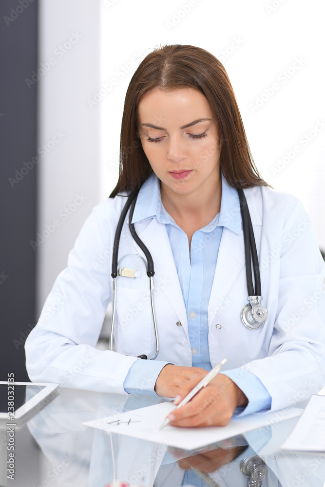 Doctor woman at work. Portrait of female physician filling up medical form while sitting at the glass desk at clinic or hospital. Medicine and healthcare concept Doctor woman at work. Portrait of female physician filling up medical form while sitting at the glass desk at clinic or hospital. Medicine and healthcare concept