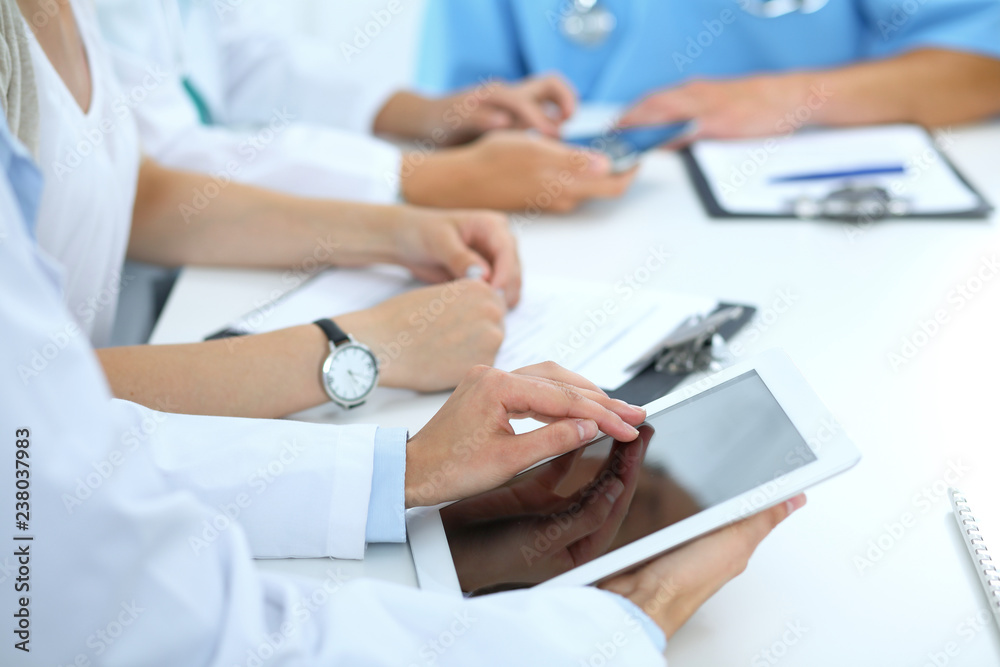 Doctor using tablet computer at medical meeting, closeup. Group of colleagues at the background Doctor using tablet computer at medical meeting, closeup. Group of colleagues at the background