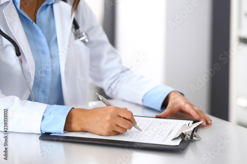Unknown doctor woman filling up medical form while sitting at the desk in hospital office  close-up of hands. Physician at work. Medicine and health care concept