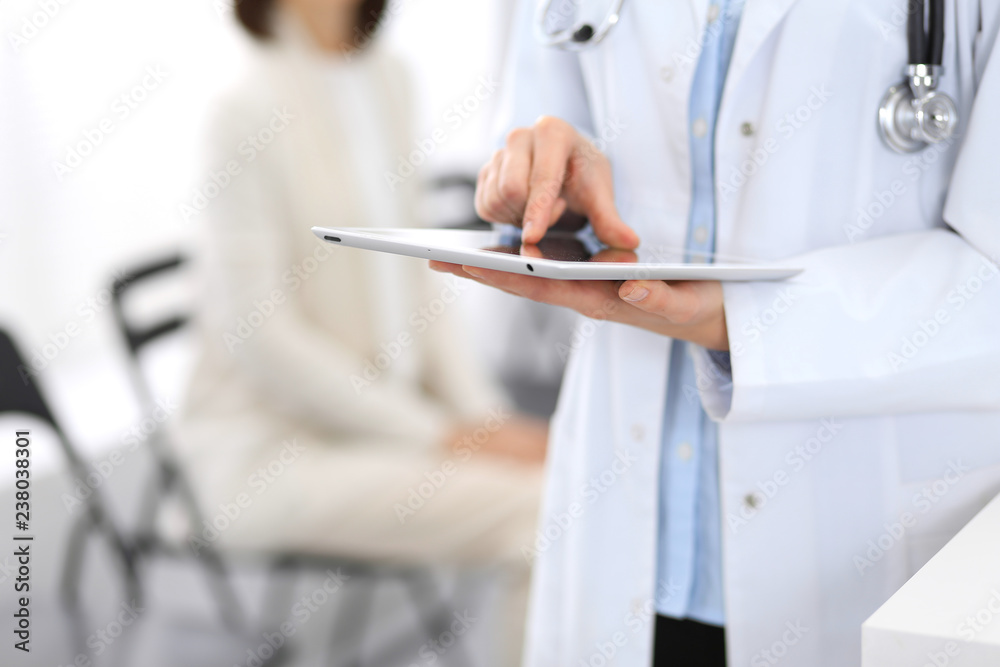 Female doctor woman using digital tablet while standing near reception desk at clinic or emergency hospital. Unknown physician at work. Medicine and patient service concept Female doctor woman using digital tablet while standing near reception desk at clinic or emergency hospital. Unknown physician at work. Medicine and patient service concept