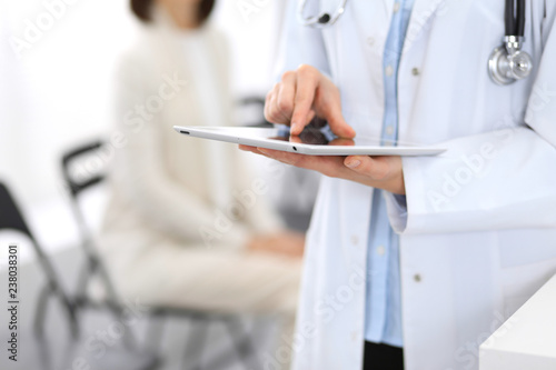 Female doctor woman using digital tablet while standing near reception desk at clinic or emergency hospital. Unknown physician at work. Medicine and patient service concept