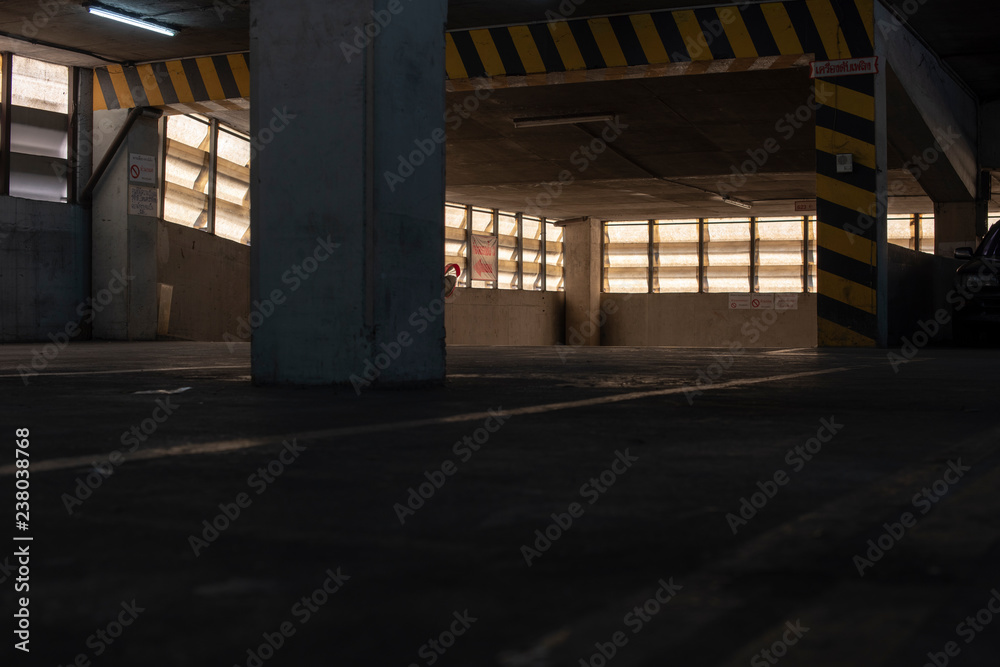A view of an old parking lot on 3th floor of a parking building in a business district with a low key. Seeing yellow and black traffic sign warning the height of the ceiling.