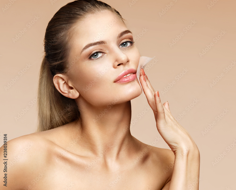 Woman cleaning face with facial cleansing wipes, removing makeup. Photo of woman with perfect skin on beige background. Beauty concept - obrazy, fototapety, plakaty 