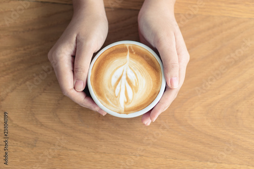 Woman hand holding a white coffee mug.  Coffee is a latte. table on the wooden table in vintage style, taken from the top view, see the froth of milk foam.