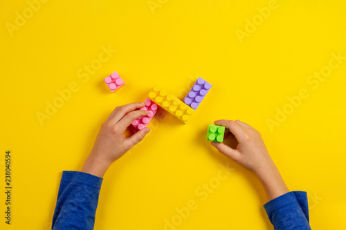 Kid hands playing with colorful plastic bricks on yellow background