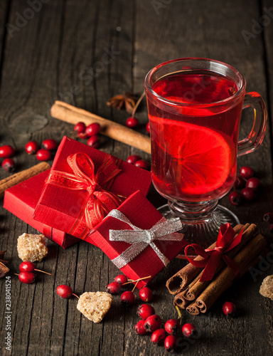 Red hot drink tea with spices, cinnamon, anise, fruits, brown sugar on an old wooden table with christmas presents. New Year and holidays concept. Mulled wine and glintwein.