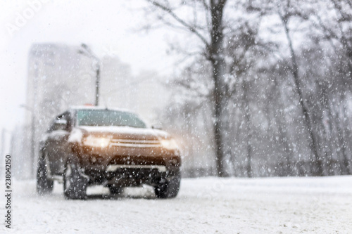 Heavy snowfall and blurred SUV awd car on road. 4wd vehicle on city street at winter. Seasonal roadside assistance concept. Copyspace