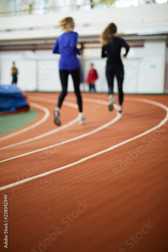 Two blurry sprinters in sportswear running down tracks on contemporary stadium
