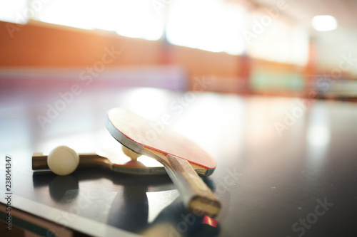 Canvas-taulu Two ping pong rackets and ball on large tennis table inside modern hall for spor