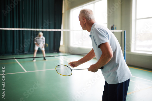 One of mature badminton players holding shuttlecock in front of racket before passing it over to his mate