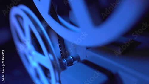 Film projector with dramatic blue lighting and selective focus. Retro film production still life. Concept of film-making. Old 8mm projector is turning off. Close-up of a reel with a film. photo