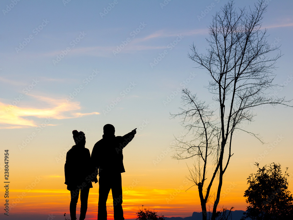 Silhouette of happy couple standing on the mountain at the sunset or sunrise time.