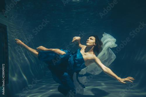 elegant pretty woman swims underwater like a free diver in a blue evening dress alone