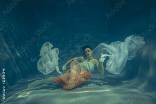 elegant slender girl swims underwater like a free diver in a white evening dress with beautiful fabric