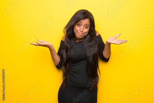 Young afro american woman on vibrant yellow background making unimportant gesture while lifting the shoulders photo
