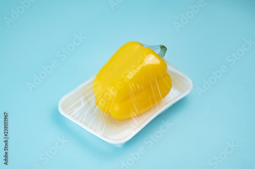 Recycling and environment concept: fresh yellow paprika in plastic package. Bell pepper wrapped in plastic clingfilm in blue background. photo