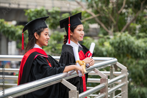 Two smiling female Asian students in graduation gown holding the diplomas with eyes looking forward photo