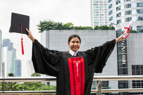 A female Asian student in graduation gown holding the diploma and graduation cap photo