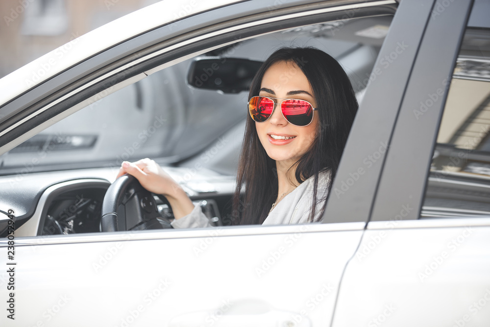 Naklejka premium Young attractive woman in the car. Woman drive an auto. Close up portrait of beautiful woman outdoors. Urban lady.