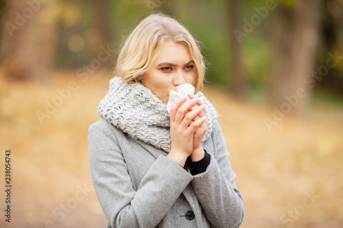 Girl sneezing in tissue. Young woman blowing her nose on the park. Woman portrait outdoor sneezing because cold and flu