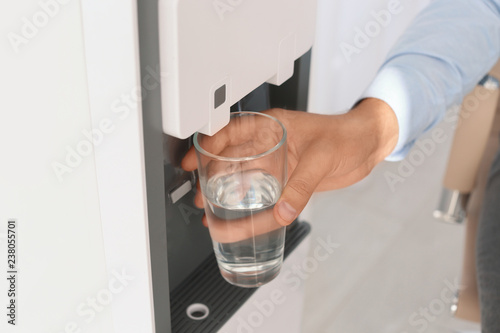 Man filling glass from water cooler at workplace, closeup