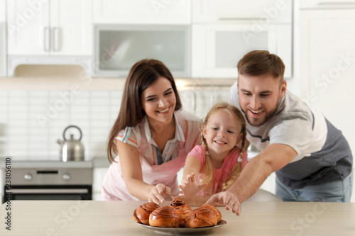 Happy family with freshly oven baked buns at table in kitchen