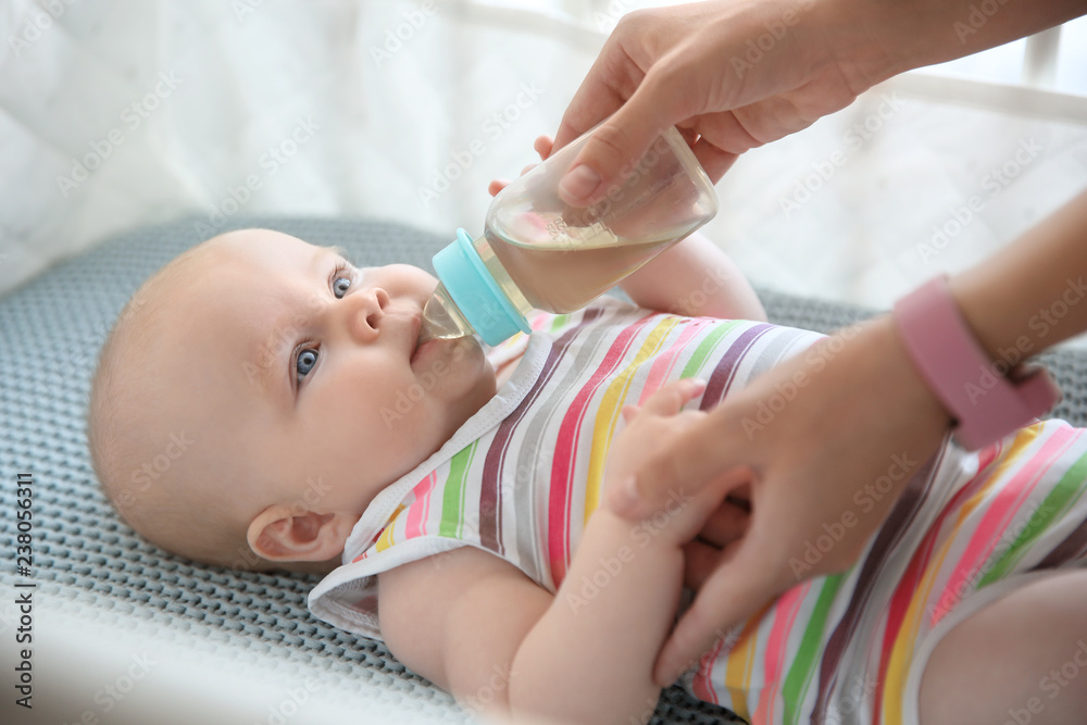 Lovely mother giving her baby drink from bottle in cot - obrazy, fototapety, plakaty 