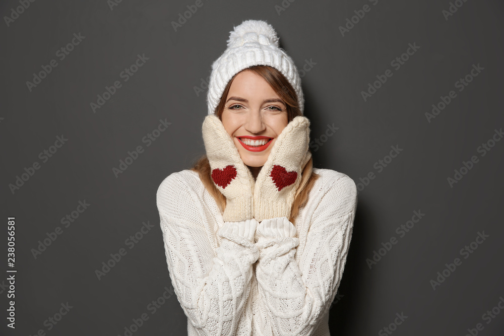 Beautiful young woman in warm sweater with hat and mittens on dark background