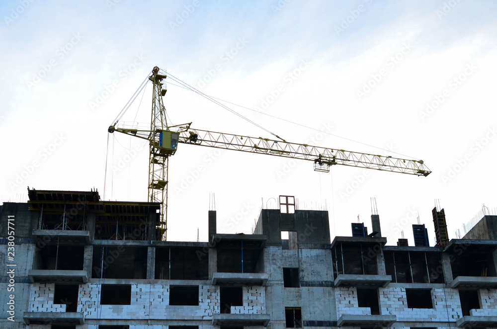 Yellow construction crane and unfinished brick house on a background of blue sky