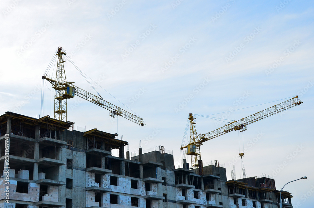 Yellow construction crane and unfinished brick house on a background of blue sky Yellow construction crane and unfinished brick house on a background of blue sky