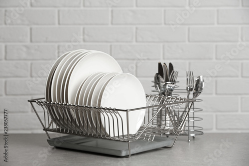 Dish rack with clean plates on table near brick wall photo