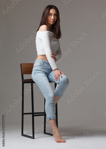stylish asian female sitting on chair isolated on gray background