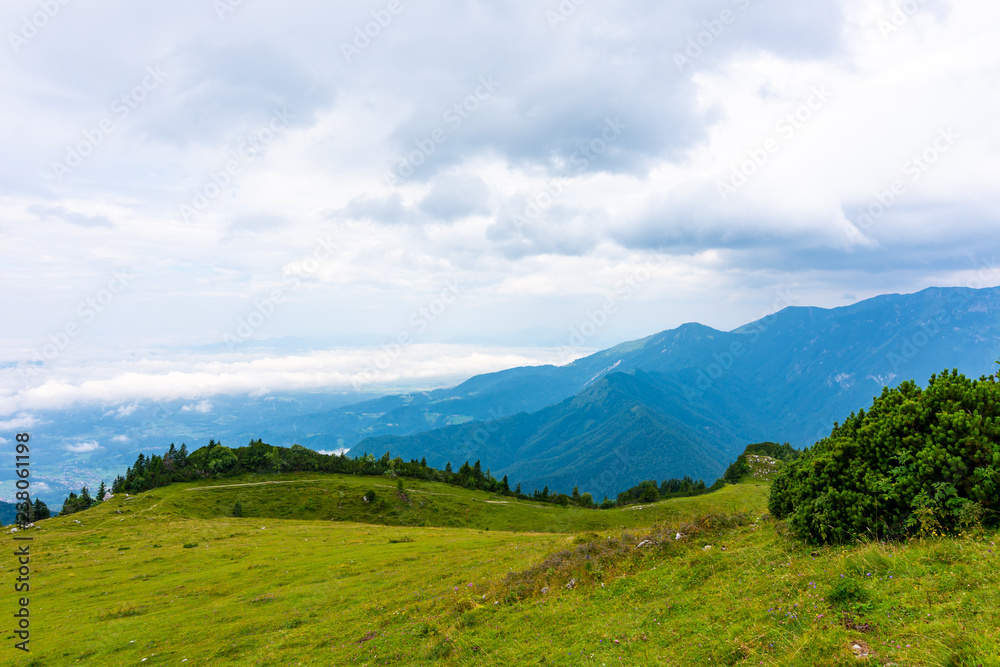 Panoramatic view to Slovenia Alps near city Kamnik. Big plateau with pasture and wooden houses. Landscape with green grass and clouds above the hill.