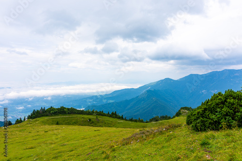 Panoramatic view to Slovenia Alps near city Kamnik. Big plateau with pasture and wooden houses. Landscape with green grass and clouds above the hill.