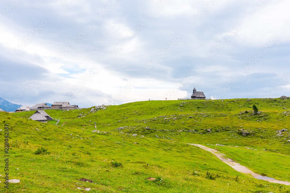 Church in the Slovenia big plateau pasture (Velika Planina). Chapel on the hill, religion symbol. Green meadow and blue sky with clouds. Plateau near the Kamnik city Church in the Slovenia big plateau pasture (Velika Planina). Chapel on the hill, religion symbol. Green meadow and blue sky with clouds. Plateau near the Kamnik city