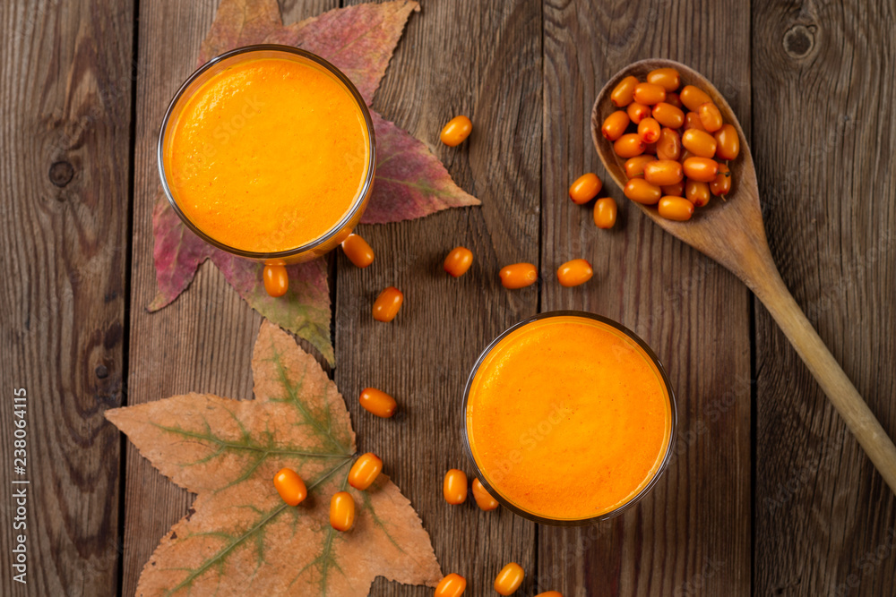 Two glasses of fresh natural sea buckthorn juice, with autumn leaves and sea buckthorn berries and wooden spoon on wooden background. Flet lay. Two glasses of fresh natural sea buckthorn juice, with autumn leaves and sea buckthorn berries and wooden spoon on wooden background. Flet lay.