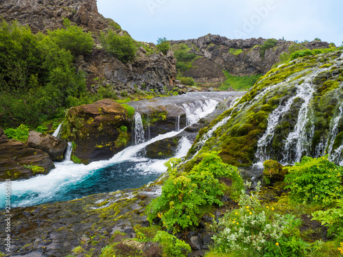 Beautiful Valley Gjain with colorful lava rocks  lush green moss and vegetation and blue water with waterfalls and cascade in south Iceland