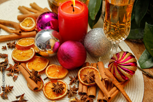 Holiday Christmas decoration with white wine, Christmas ball, candle, dried orange, anise stars and sticks of cinnamon. Wooden table and vintage background.