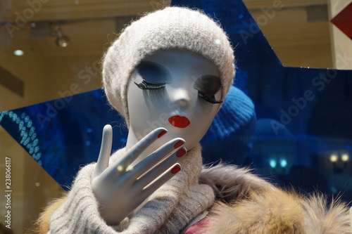 Mannequin with long eyelashes, red lips and red nail in white knitted hat