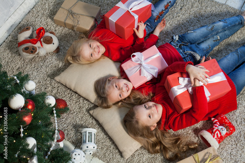Fotografia two small girls blondes lie near a Christmas tree gifts new year holiday
