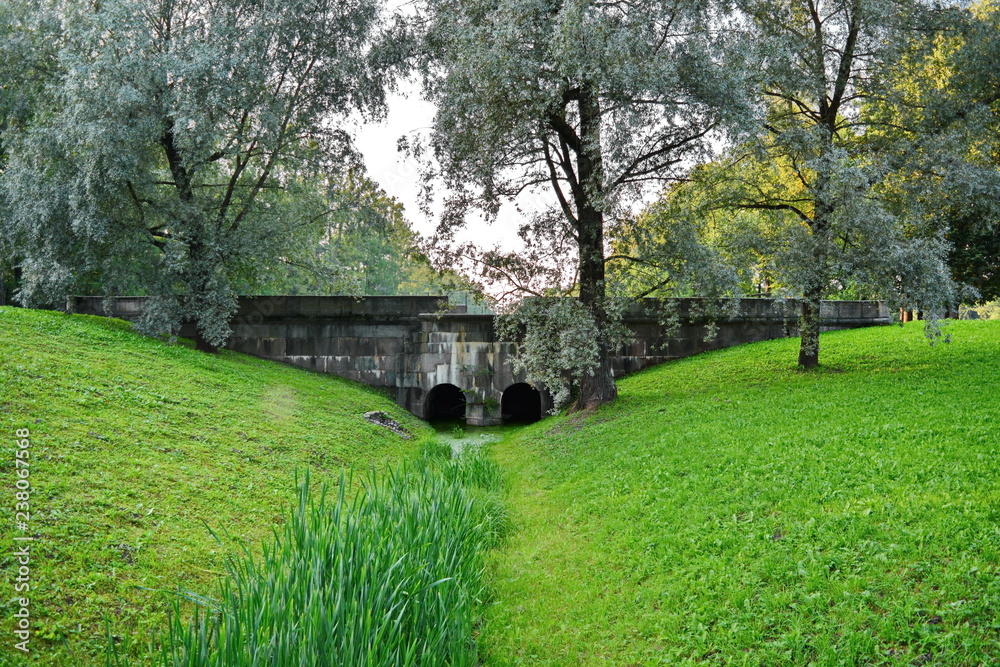 empty deserted stone bridge in an old Park over a dry Creek overgrown with green grass empty deserted stone bridge in an old Park over a dry Creek overgrown with green grass