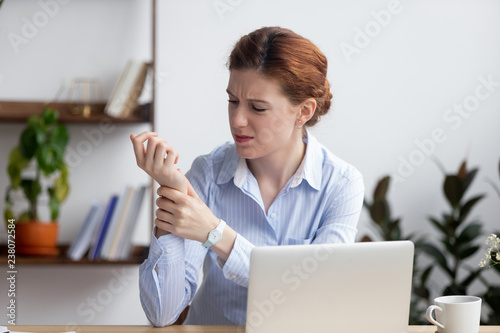 Businesswoman sitting at desk in office touch wrist feels pain. Unhealthy upset female having carpal tunnel syndrome because of active and long-term use of the keyboard and mouse in the wrong posture