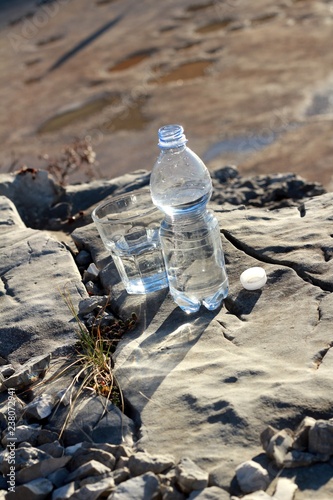 Una botella de agua mineral,con vaso sobre una roca