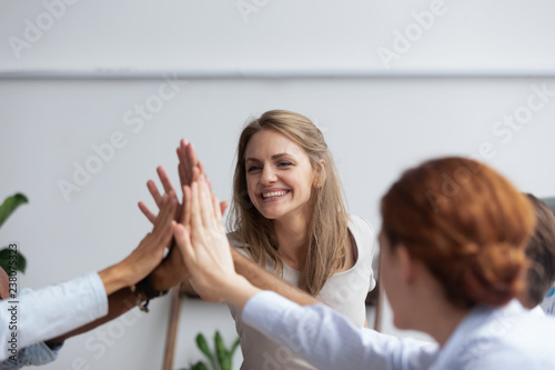 Diverse multinational businessmen and businesswomen gathered together in boardroom before seminar giving high five expressing respect team spirit and unity, focus on attractive happy millennial female