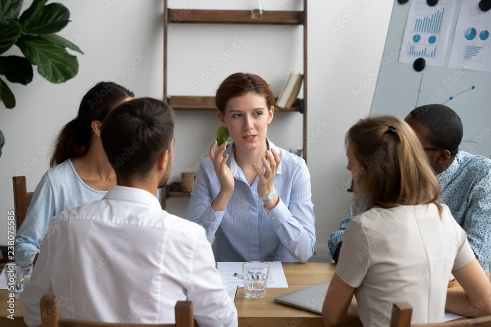 Five diverse people brainstorming sitting around desk in briefing at boardroom. Attentive multiracial employees listening company executive manager or business trainer, coaching and mentoring concept Five diverse people brainstorming sitting around desk in briefing at boardroom. Attentive multiracial employees listening company executive manager or business trainer, coaching and mentoring concept