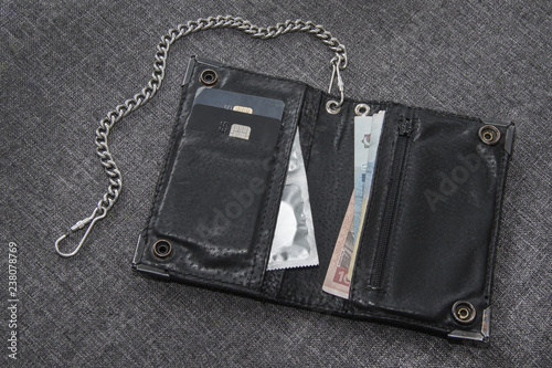 Men's black leather wallet on the chain. There are payment cards, money and condoms in the wallet.