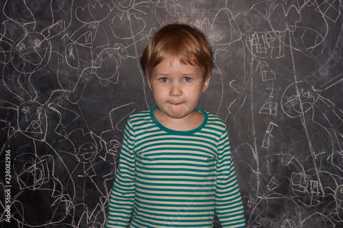 A child against a chalk board with little men painted by this kid. Pensive boy in a striped T-shirt