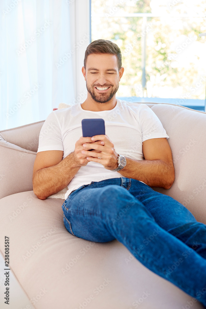Young man text messaging while sitting on couch at home Young man text messaging while sitting on couch at home