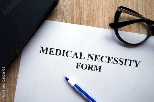 Medical necessity form, pen and glasses on desk