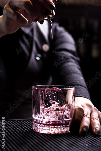 Bartender making refreshing coctail on a bar background. Dark moody style. Ice in tha glass